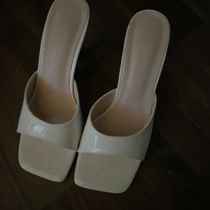 Vita klackar med fyrkantig tå - Säljer ett par stilrena vita sandaler med hög klack och fyrkantig tå. Skorna har en bred rem framtill med krokodilpräglat mönster och öppen häl. Perfekta för dig som vill ha en trendig och elegant look. Använda en gång🤍🌸