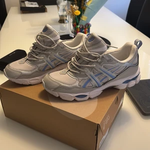 Asics utility - Säljer ett par fräscha Asics sneakers i grått och vitt med ljusblå detaljer. Skorna har snörning, rund tå och platt sula. Perfekta för dig som gillar sportig stil och vill ha bekväma skor till vardagen.