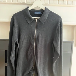 Tröja  - Svart stickad tröja från Riley med hel dragkedja framtill och klassisk krage. Tröjan har lång ärm och är enkel att matcha till olika outfits. Perfekt för kyligare dagar.