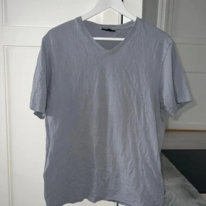 Ljusgrå v-ringad t-shirt - En enkel och stilren ljusgrå t-shirt med v-ringning i regular fit. Inte jättemycket använd! Axelbredd 45cm, längd 68cm.