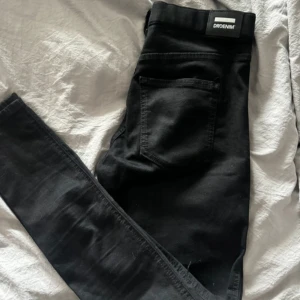 Svarta jeansbyxor från Drdenim - Svarta jeansbyxor från Drdenim med klassisk femficksdesign och smal passform. Byxorna har hög midja och är tillverkade i stretchigt material för extra komfort. Perfekta för en stilren och enkel look.
