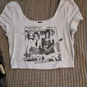 Vit croppad t-shirt med anime-tryck - Cool vit croppad t-shirt med svart anime-inspirerat tryck och text som 'PASSION BURNING', 'SHINING STARS' och 'ROCK PUNK'. Rund halsringning och korta ärmar. Perfekt för dig som gillar unik streetstyle. Passar alternativa stilar. Knappt använd