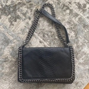 Svart väska - Säljer en svart väska med kedjedetaljer i skin/ mocka på framsidan
