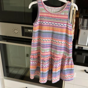 Färgglad mönstrad sommarklänning - Säljer en söt och färgglad ärmlös klänning med olika mönster i rosa, blått, orange, grönt och vitt. Klänningen har rund halsringning och är i mjukt bomullsmaterial, perfekt för varma dagar.
