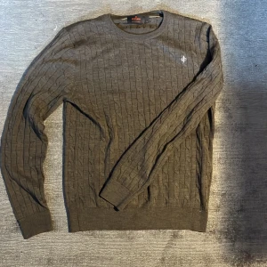 Grå kabelstickad tröja från Morris - OBS priset ej hugget i sten. Säljer en grå kabelstickad tröja från Morris i 100% merinoull. Tröjan har rund halsringning, en liten broderad logga på bröstet. Perfekt för dig som gillar klassisk och stilren design.