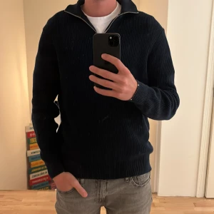 Mörkblå stickad tröja med halv dragkedja - Säljer en mörkblå stickad tröja med halv dragkedja i halsen. Tröjan har lång ärm och ribbad struktur, perfekt för lager-på-lager. Storleken är medium och den är i färgen marinblå, super bra tröja som passar till både tishor under eller skjortor:)