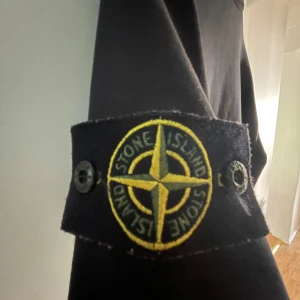 Svart sweatshirt från Stone Island - Säljer en svart långärmad sweatshirt från Stone Island med den klassiska loggan på vänster ärm. Tröjan har rund halsringning och är tillverkad i mjukt material. Perfekt för en stilren och avslappnad look. Ser soltblekt ut på bilderna men man ser ej det i verkligen. Pris kan diskuteras! 