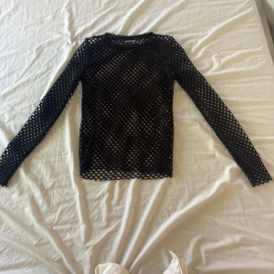 Svart meshtröja från Weekday - Säljer en svart långärmad meshtröja från Weekday. Tröjan är tight och helnätad vilket ger en cool och edgy look. Perfekt att styla lager på lager eller som statement-plagg.