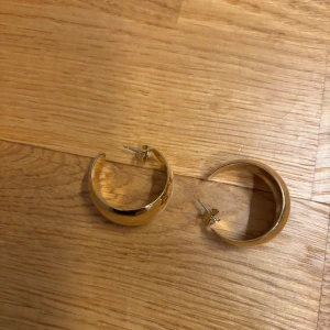 Guldiga chunky hoops örhängen - Säljer ett par chunky hoops örhängen i guldig metall. De är halvrunda och har en slät, blank yta som ger en snygg och modern look. Perfekta för att lyfta vilken outfit som helst!