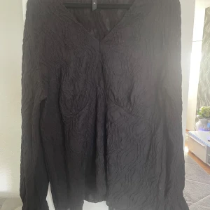 Svart långärmad blus med struktur  - Säljer en svart långärmad blus i storlek XL. Blusen har en snygg strukturerad yta och v-ringning. Perfekt för dig som gillar stilrena plagg med det lilla extra.