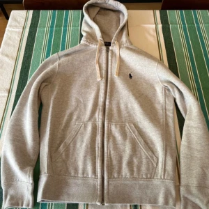 Grå hoodie från Polo Ralph Lauren - Säljer en grå hoodie från Polo Ralph Lauren med dragkedja och huva. Den är i extremt fint skick, nypris = 2300 kr mitt = 599 kr, pris kan diskuteras!