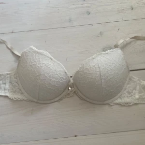 Vit spets-bh från H&M - Säljer en vit bh från H&M med vadderade kupor och spetsdetaljer. Bh:n har bygel och justerbara axelband. Perfekt för dig som vill ha en enkel men ändå fin bh med spets.
