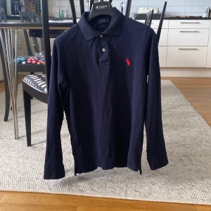 Mörkblå pikétröja från Polo Ralph Lauren - Säljer en klassisk mörkblå långärmad pikétröja från Polo Ralph Lauren i modellen Custom Fit. Strl S, hör av er om ni har några funderingar!