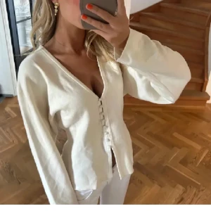 Vit kofta med knappar - Säljer en stilren vit kofta med v-ringning och knappar framtill. Koftan har lång ärm och är tillverkad i ett mjukt material som passar perfekt till många olika outfits. Passar nån som bär xs-s