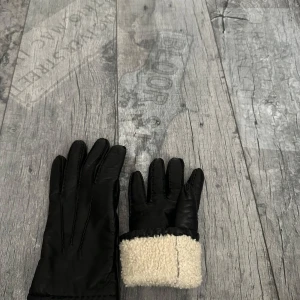 Svarta skinnhandskar med foder - Svarta handskar i skinn med mjukt, ljust foder vid handleden. Snygg och stilren design med klassisk passform. Perfekta för kyliga dagar.