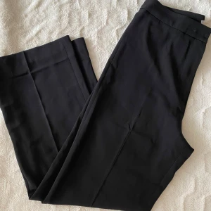 Svarta kostymbyxor från H&M - Stilrena svarta kostymbyxor från ACG med klassisk passform och raka ben. Byxorna har dold dragkedja och knapp i midjan. Perfekta för en dressad look och passar till skjorta eller kavaj.