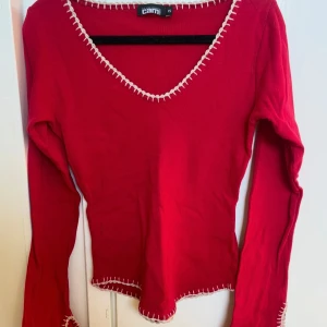 Röd långärmad tröja med vit kontrastsöm - Säljer en röd långärmad tröja från Cami med vit kontrastsöm längs v-ringningen, ärmsluten och nederkanten. Tröjan har en figurnära passform🫶🏼