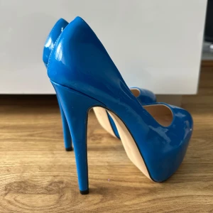 Blåa pumps med hög klack - Säljer ett par glansiga blåa pumps med hög klack och rund tå. Skorna har en klassisk design och är tillverkade i syntetmaterial med en slät finish. Perfekta för dig som vill sticka ut med färg. Oanvända storlek 36