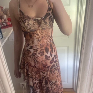 Leopardmönstrad långklänning med slits - Säljer en långklänning med leopardmönster i bruna och beige toner. Klänningen har smala axelband som korsas i ryggen och en hög slits på sidan. Materialet är lätt och följsamt, perfekt för sommardagar.