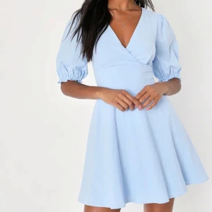 Ljusblå kortklänning med puffärmar och v-ringning - Supersöt ljusblå klänning med v-ringad omlottfront, puffiga kortärmar och knytning i ryggen. Super fin! Helt ny med prislapp!