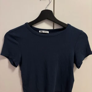 Mörkblå croppad t-shirt från Zara - En mörkblå croppad t-shirt från Zara. Modellen har rund halsringning och korta ärmar. Lite mindre i storleken.