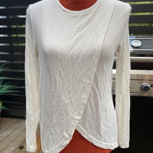 Vit omlott långärmad tröja small - Långärmad tröja med en omlottdesign framtill. Den har en rund halsringning och en rak passform. Längd: 65 cm ﻿Bystvidd: 47 cm  Inga bilder när den sitter på mig! Katter finns i hemmet!