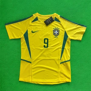 Brasilien Ronaldo 9 fotbollströja Nike - Gul Brasilien fotbollströja från Nike med gröna detaljer, nummer 9 och Ronaldo på ryggen. Klassisk design med korta ärmar, rund hals och broderat landslagsemblem på bröstet. Tillverkad i lätt och ventilerande material, perfekt för match eller träning.