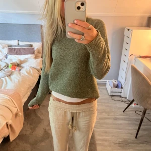 Grön stickad tröja med lång ärm - Mysig grön stickad tröja med rund hals och långa ärmar. Tröjan har en enkel och stilren design, perfekt att slänga på sig när det är kyligt. Den är lite loose i passformen och har ribbade muddar vid ärmslut och nederkant.