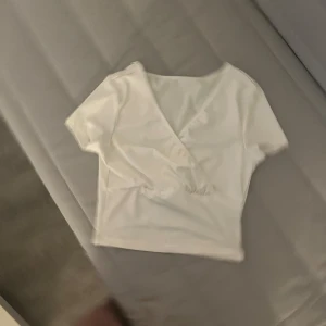 Vit omlottopp med v-ringning - Säljer en stilren vit omlottopp med korta ärmar och v-ringad hals. Toppen har en enkel och fräsch design som passar perfekt till jeans eller kjol. Materialet känns mjukt och följsamt mot huden. Perfekt för dig som gillar minimalistisk stil.