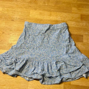 Blommig volangkjol från Lindex - Supersöt blå kortkjol från Lindex med vita små blommor och volangkant nertill!