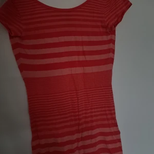 Röd- och rosarandig kortklänning - Kortärmad klänning i storlek 34 med röda och rosa horisontella ränder. Modellen är figurnära och har en rund halsringning. Perfekt för dig som gillar färg och mönster med en enkel, ungdomlig stil.