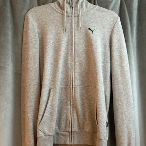 Grå hoodie från Puma med dragkedja - Snygg gråmelerad hoodie från Puma med hel dragkedja och huva med snörning. Använd fåtal gånger men är som helt ny!