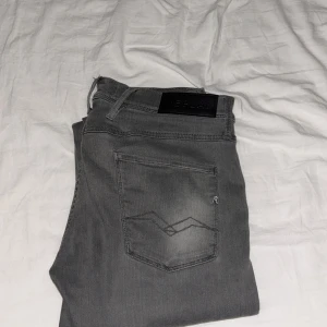 Replay Anbass Slim fit Jeans 33/32 - Snygga Replay Anbass jeans i grå tvätt med klassisk femficksdesign och diskreta slitningar. Jeansen har normal passform och raka ben, med Replay-logga på bakfickan och midjebandet. Perfekta för en avslappnad och stilren look. 33/32!