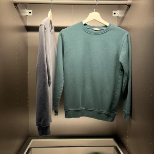 Blå och grön sweatshirt i bomull - En stilren blågrön sweatshirt med rund hals och ribbade muddar. Tröjan är enkel och clean i modellen, perfekt för dig som gillar en chill och avslappnad vibe. Tillverkad i mjuk bomull som känns skön mot huden. Passar dig som vill ha en basic men snygg tröja. Jätte bra skick nästan helt nya! Vet dock inte vart dom e ifrån då jag har klippt bort lappen! Finns i mörkblå oxå! 