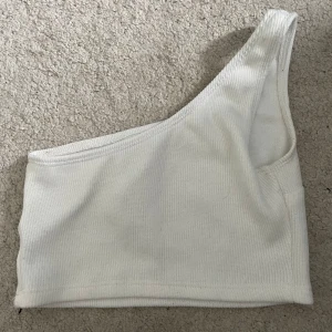 Vit ribbad oneshoulder topp från Shein - Snygg vit ribbad topp med oneshoulder-design från Shein. Perfekt för dig som gillar en stilren och modern look. Toppens ribbade material ger en extra touch och sitter skönt mot kroppen.
