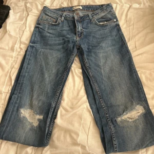 Wide jeans från Gina Tricot, blå, stl 40 - Blå jeans från Gina Tricot i modellen 'perfect jeans', storlek 40. Byxorna har breda ben, slitna detaljer vid knäna och klassisk femficksdesign. Materialet är en mix av bomull, polyester och elastan för en skön känsla och lite stretch.