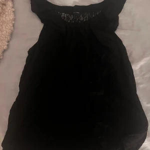 Fest blus med spets och paljetter/pärlor - Supersnygg svart blus med detalj på framsidan och glittriga paljettdetaljer/pärldetaljerad öppen rygg. Blusen är ärmlös och har en luftig. Perfekt för dig som gillar att sticka ut med coola detaljer och en elegant vibe. Festlig topp