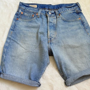 Levi's  ljusblå jeansshorts W28 - Klassiska ljusblå jeansshorts från Levi's modell 501 med fem fickor, uppvikta benslut och ikonisk läderpatch bak. Perfekta för en chill sommarlook med avslappnad passform och tidlös denimstil.