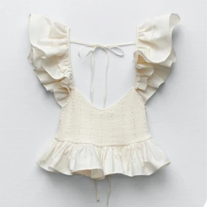 Vit volangtopp från Zara - Supersöt vit topp från Zara med volangärmar och smockad överdel. Toppen har knytning i ryggen och volang nertill som ger en romantisk vibe. Perfekt för sommardagar och passar till både jeans och kjol. Luftigt material och riktigt trendig modell.
