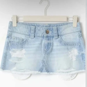 Populär jeans kjol från Gina 14+ - Snygg ljusblå jeanskjol i kort modell med slitna detaljer och rå kant nertill. Klassisk femficksdesign och knapp framtill. Perfekt för dig som gillar en avslappnad och trendig stil.