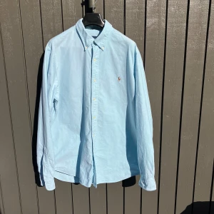 Ljusblå skjorta från Ralph Lauren XL - Klassisk ljusblå skjorta från Ralph Lauren! Stilren skjorta inför sommaren som är använd ett par gånger. Skjortan har en fläck på vänster sidan av skjortan som knappt syns. Bara att skriva vid minsta fundering.🤗Priset är inte hugget i sten. 