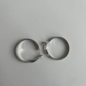 Silvriga hoops örhängen - Ett par klassiska silvriga hoops örhängen i rund form. De är blanka och har en enkel, stilren design som passar till det mesta. Lätta att ta på med smidig låsning. Perfekta för dig som gillar minimalistiska smycken.
