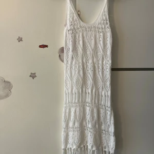 Vit stickad klänning med fransar - Superfin vit stickad kortklänning med snyggt mönster och fransar längst ner. Ärmlös modell med rundad urringning, perfekt för sommarens varma dagar. Ger en chill och bohemisk vibe, lätt att styla över bikini eller med sandaler.