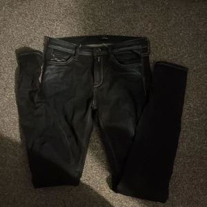 Svarta Replay jeans  - Säljer ett par svarta Replay jeans. Klassisk femficksmodell med snygga kontrastsömmar och Replay-logga på fickan. Jeansen är i stretchigt denim som sitter tajt och bekvämt. Perfekta för dig som gillar en stilren och modern look. De är inte alls använda ett fåtal gånger.