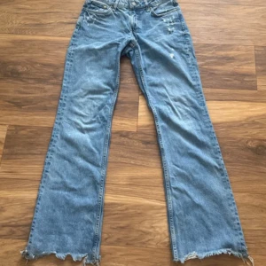 Blå midwaist flare jeans  - Säljer ett par ljusblå midwaist flared jeans med några slitningar. Jeansen har klassisk femficksmodell och normal passform. 