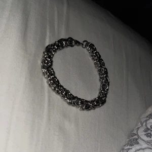 Tjockt silverfärgat kedjearmband - Säljer ett chunky armband i silverfärg med flätad kedjedesign. Armbandet har en robust känsla och stängs med ett klassiskt karbinlås. Perfekt för dig som gillar statement-smycken och vill sticka ut lite extra.