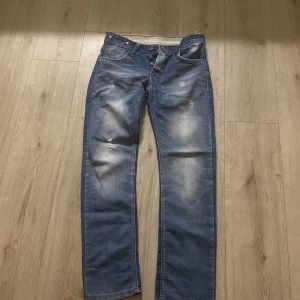 Blå jeans från Armani, straight fit - Snygga blå jeans från Armani i straight fit med slitna detaljer och ljusa partier på låren. Klassisk femficksmodell med knappgylf och coolt tvättad look. Perfekta för dig som gillar en avslappnad men stilren vibe.