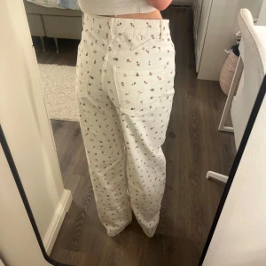 Blommiga vita wide jeans  - Säljer ett par vita högmidjade jeans med gulligt blommigt mönster köpta från Kappahl och aldrig använda!