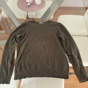 Mörkgrön stickad tröja  - En enkel och stilren mörkgrön stickad tröja med rund halsringning och långa ärmar. Tröjan har ribbade muddar vid ärmslut och nederkant, perfekt för lager-på-lager under kyliga dagar. Säljer pga för liten. Mycket bra skick.