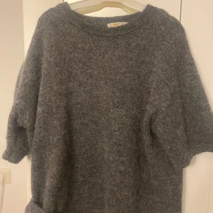 Grå stickad tröja från Gina Tricot - Mysig grå stickad tröja från Gina Tricot med kortare ärmar och rund halsringning. Tröjan har en loose fit och är perfekt för lager-på-lager under kyliga dagar. Enkel och stilren design som funkar till allt.